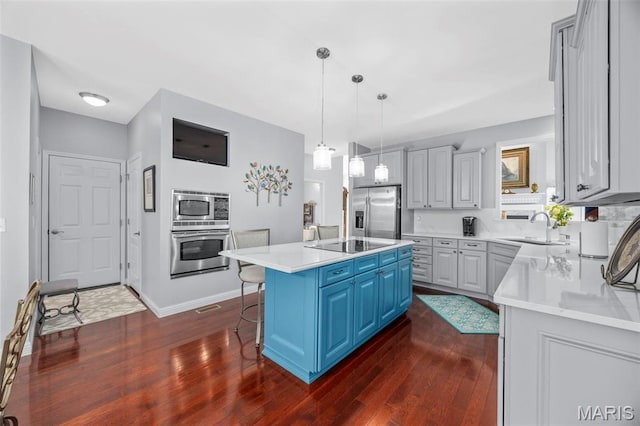 kitchen with stainless steel appliances, a sink, dark wood-type flooring, blue cabinets, and a kitchen island