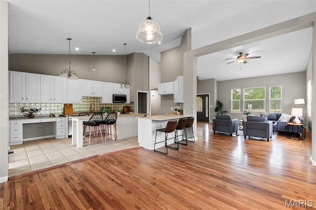 122 Morgan Lake Rd, De Soto, MO 63020 - kitchen featuring stainless steel microwave, light wood-type flooring, a kitchen bar, decorative backsplash, and high vaulted ceiling