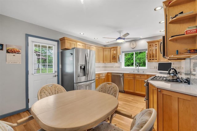 kitchen with stainless steel appliances, a sink, decorative backsplash, a ceiling fan, and light countertops