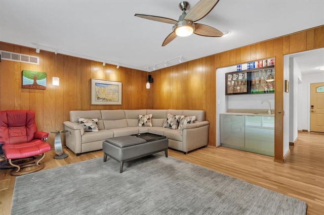 living area featuring track lighting, wood finished floors, a ceiling fan, and wood walls