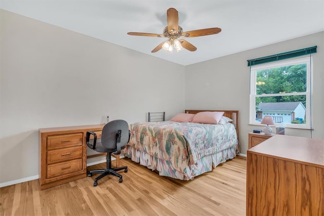 bedroom featuring light wood-style floors, baseboards, an office area, and ceiling fan