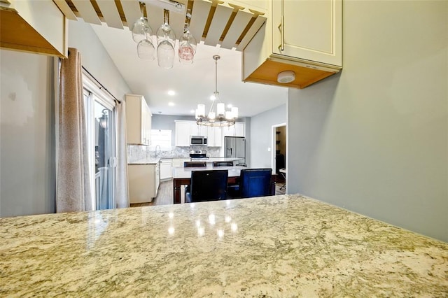 491 Cypress Creek Ln, Imperial, MO 63052 - kitchen with appliances with stainless steel finishes, a chandelier, light stone countertops, a sink, and backsplash