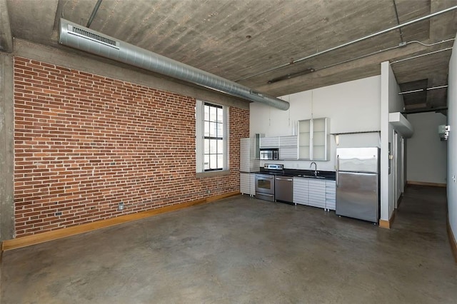 kitchen with stainless steel appliances, concrete floors, dark countertops, brick wall, and white cabinets