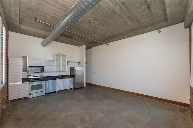 kitchen featuring appliances with stainless steel finishes, finished concrete flooring, dark countertops, white cabinetry, and baseboards
