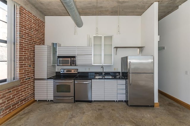 kitchen with appliances with stainless steel finishes, a sink, concrete flooring, dark countertops, and brick wall