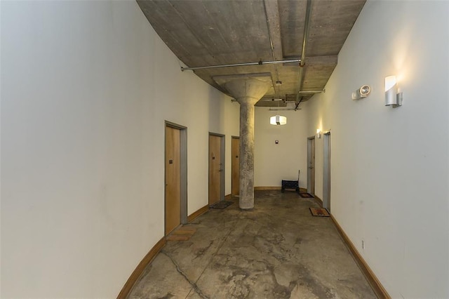 corridor with concrete flooring, a high ceiling, and baseboards