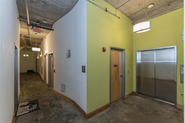 corridor with elevator, concrete flooring, a towering ceiling, and baseboards