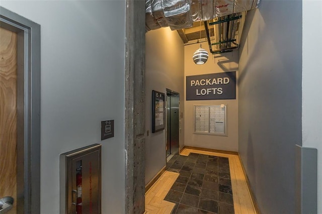 hallway with a high ceiling, elevator, and baseboards