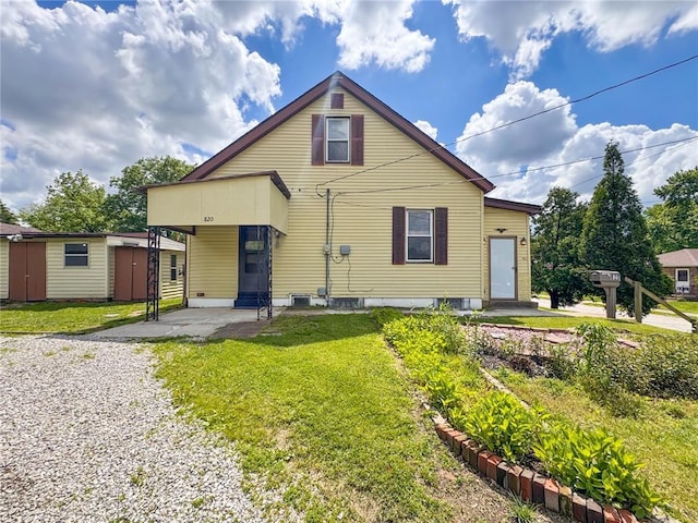 back of house with a lawn, an outbuilding, an attached carport, gravel driveway, and central AC