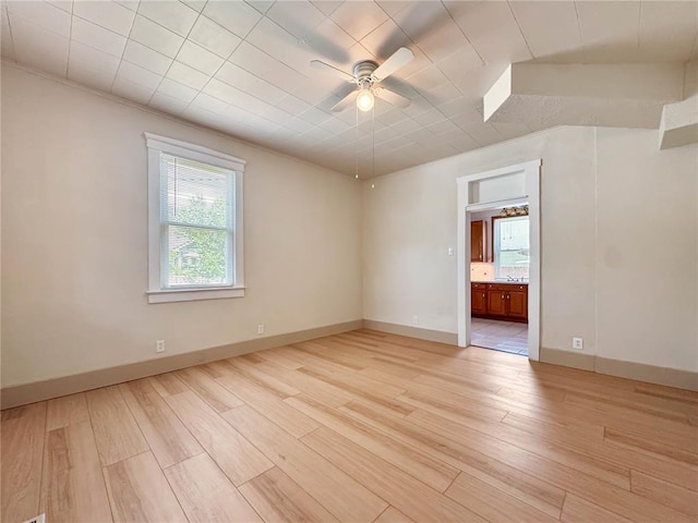 empty room with light wood finished floors, a ceiling fan, and baseboards