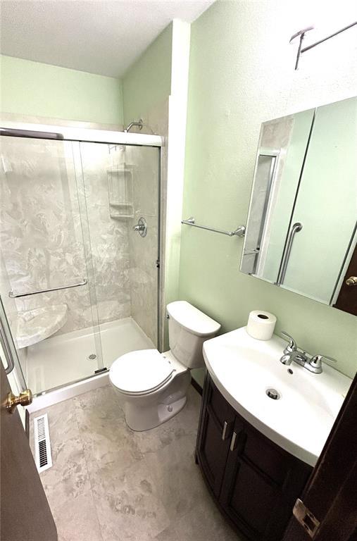 full bathroom featuring a stall shower, toilet, and vanity