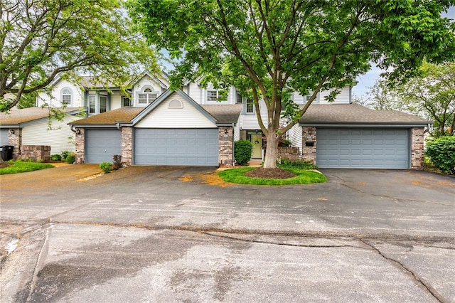view of property hidden behind natural elements with asphalt driveway and roof with shingles