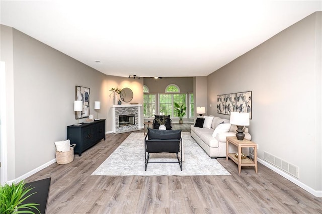 living area featuring light wood finished floors, a stone fireplace, and baseboards