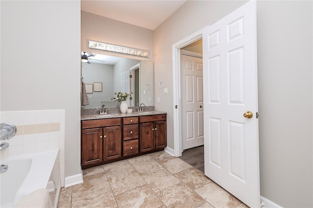 full bathroom featuring ceiling fan, a garden tub, double vanity, and baseboards