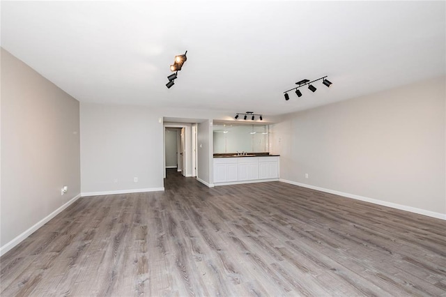 unfurnished living room with wood finished floors, baseboards, bar area, and track lighting