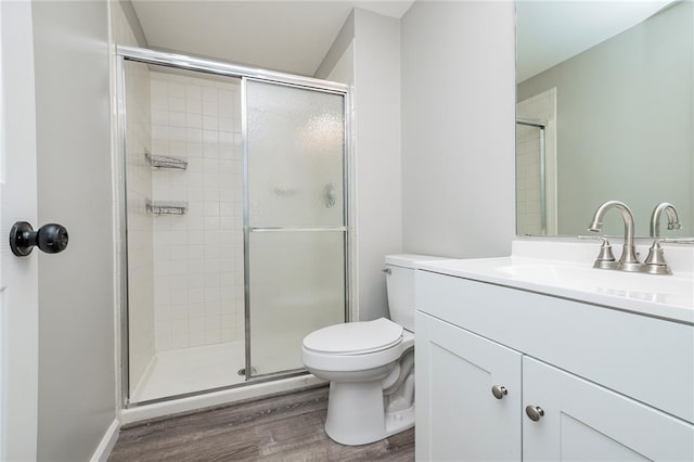 bathroom featuring wood finished floors, a stall shower, toilet, and vanity