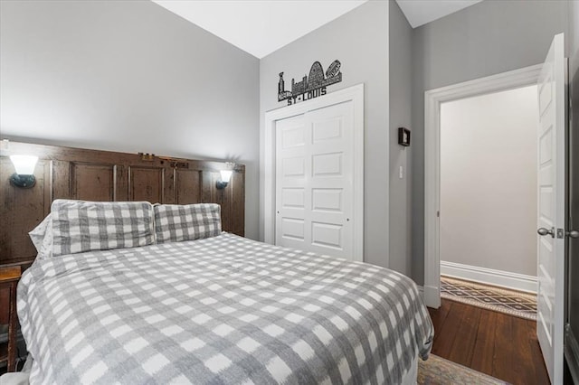 bedroom with wood finished floors, baseboards, a closet, and vaulted ceiling