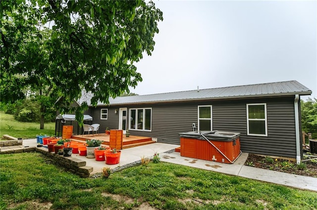 back of property with a hot tub, metal roof, a yard, and a wooden deck