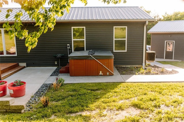 rear view of property with a hot tub, central AC unit, metal roof, a patio area, and a lawn