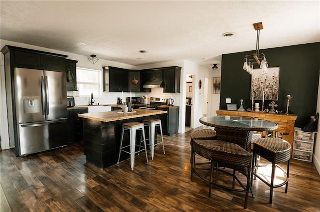 kitchen featuring appliances with stainless steel finishes, under cabinet range hood, dark cabinets, and dark wood-style floors