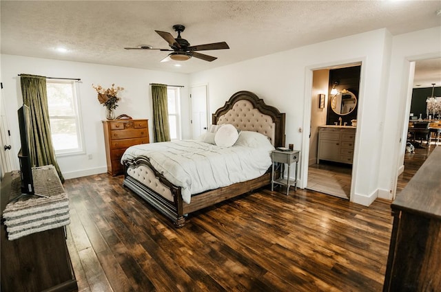 bedroom featuring dark wood-type flooring, a textured ceiling, baseboards, ensuite bath, and a ceiling fan