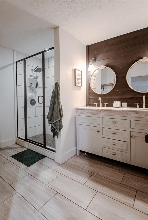 bathroom featuring a shower stall, double vanity, baseboards, and a textured ceiling