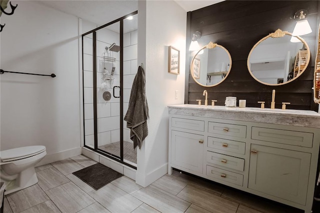bathroom featuring a stall shower, toilet, double vanity, baseboards, and wood finish floors