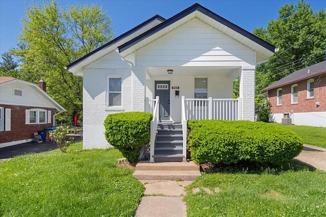 bungalow-style home featuring brick siding, covered porch, central AC, and a front yard
