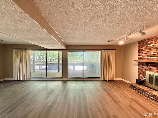 8305 Brouk Dr, Cedar Hill, MO 63016 - unfurnished living room with a textured ceiling, rail lighting, baseboards, wood finished floors, and a fireplace