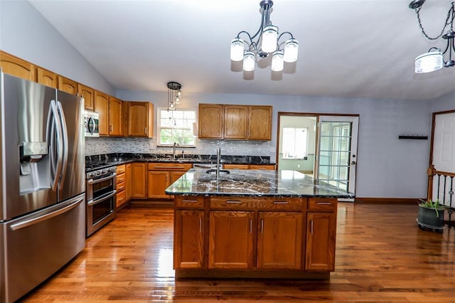 kitchen featuring appliances with stainless steel finishes, wood finished floors, backsplash, lofted ceiling, and a center island with sink