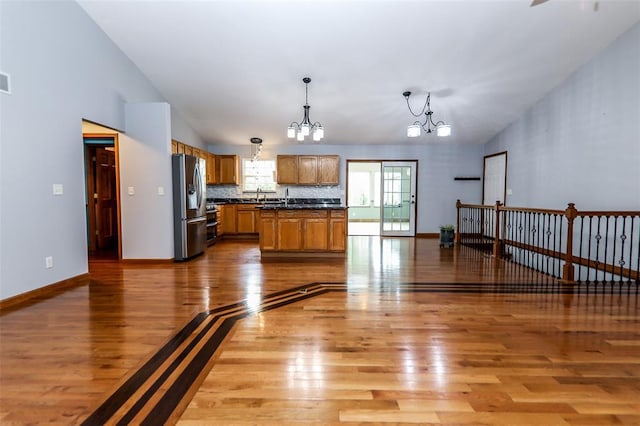 kitchen with appliances with stainless steel finishes, a chandelier, light wood-type flooring, dark countertops, and hanging light fixtures