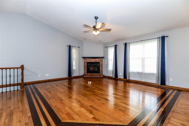 unfurnished living room with lofted ceiling, wood finished floors, a brick fireplace, a ceiling fan, and baseboards