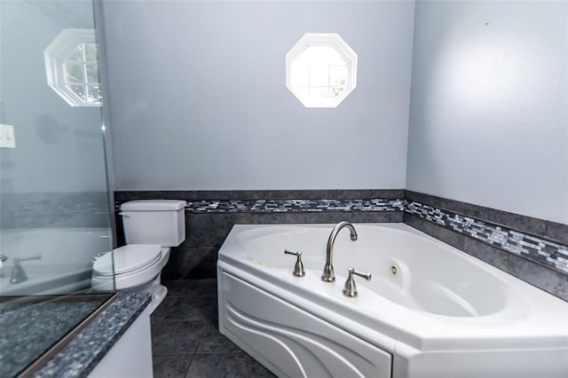 bathroom with a tub with jets, tile patterned flooring, toilet, tile walls, and wainscoting