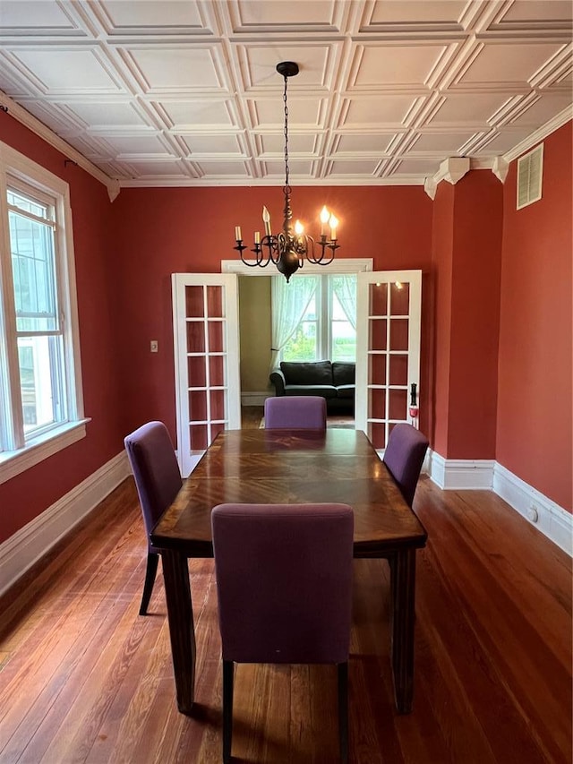 dining room featuring a chandelier, baseboards, light wood-type flooring, an ornate ceiling, and french doors
