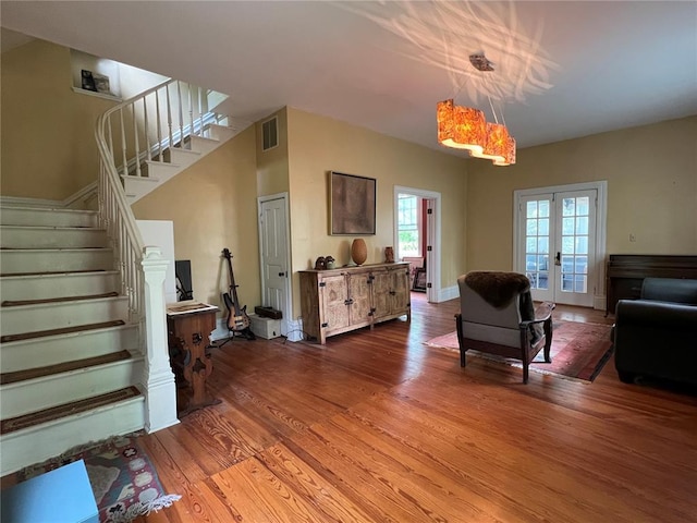living room featuring wood finished floors, stairs, french doors, and a chandelier