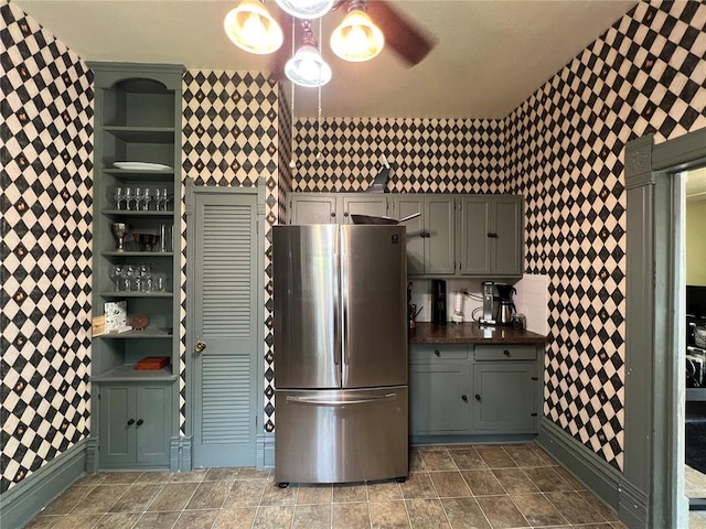kitchen with freestanding refrigerator, wallpapered walls, open shelves, gray cabinets, and dark countertops