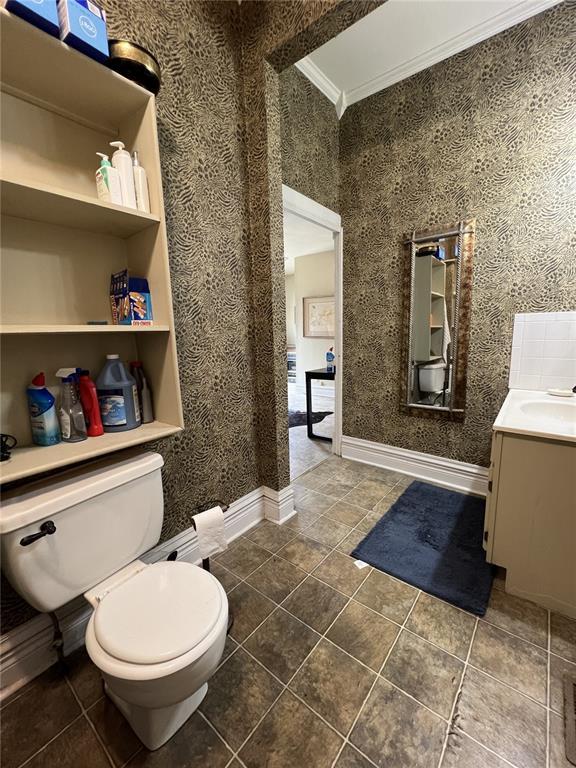 bathroom featuring toilet, tile patterned floors, crown molding, vanity, and baseboards