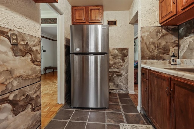 8909 Tutwiler Ave, Berkeley, MO 63134 - kitchen featuring freestanding refrigerator, light countertops, a textured wall, and brown cabinetry