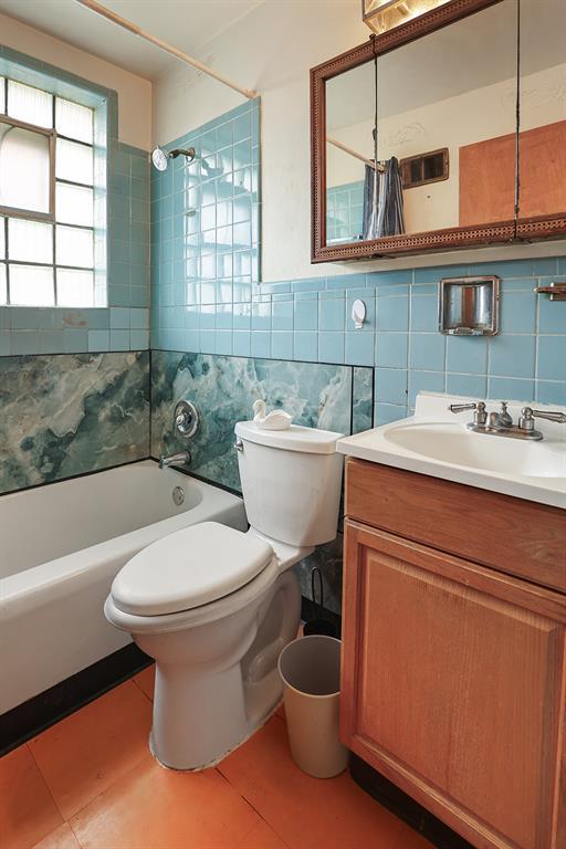 8909 Tutwiler Ave, Berkeley, MO 63134 - bathroom with tile walls, bathing tub / shower combination, toilet, tile patterned flooring, and vanity