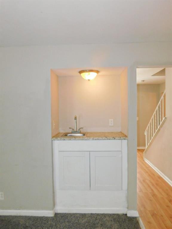 indoor wet bar featuring baseboards, stairs, and light wood-type flooring