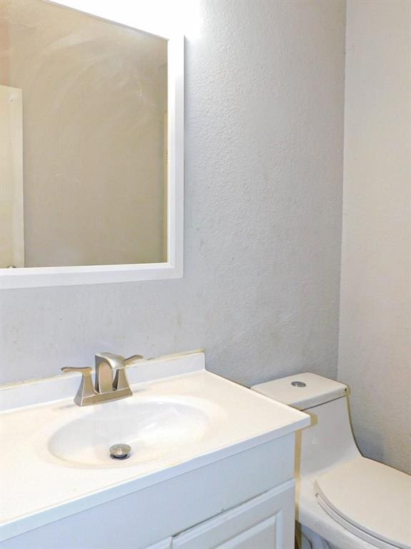 half bath with toilet, vanity, and a textured wall