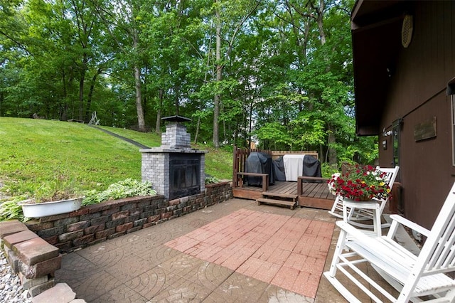view of patio featuring an outdoor brick fireplace, a wooden deck, and view of scattered trees