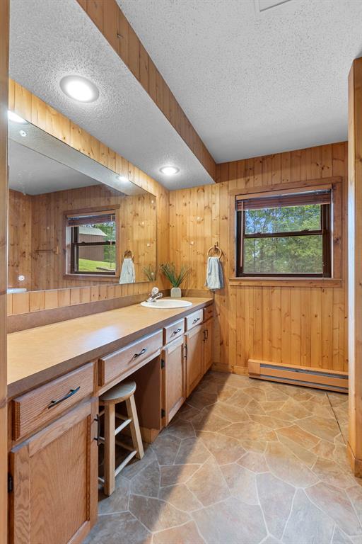 bathroom with a baseboard heating unit, a textured ceiling, stone flooring, wood walls, and vanity