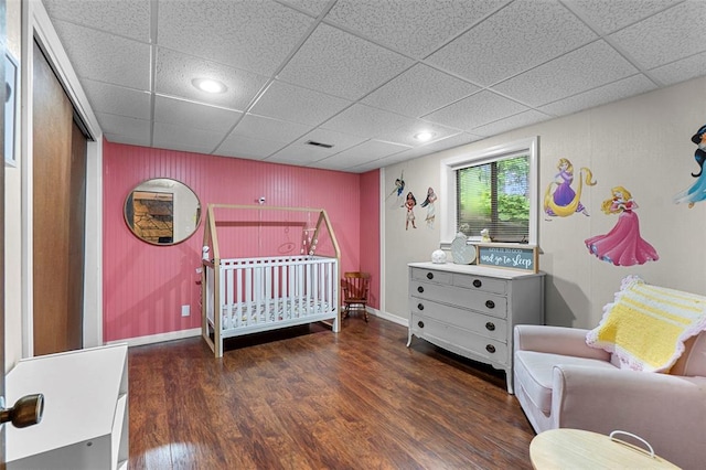bedroom featuring wood finished floors, a drop ceiling, and a nursery area