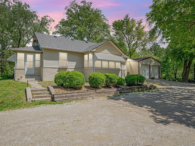 view of front of home with entry steps, a garage, an outbuilding, a shingled roof, and driveway