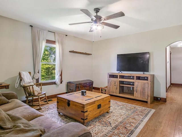 living room featuring arched walkways, ceiling fan, wood finished floors, and baseboards