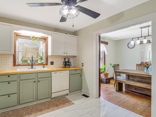 kitchen with green cabinetry, dishwasher, butcher block counters, backsplash, and a sink