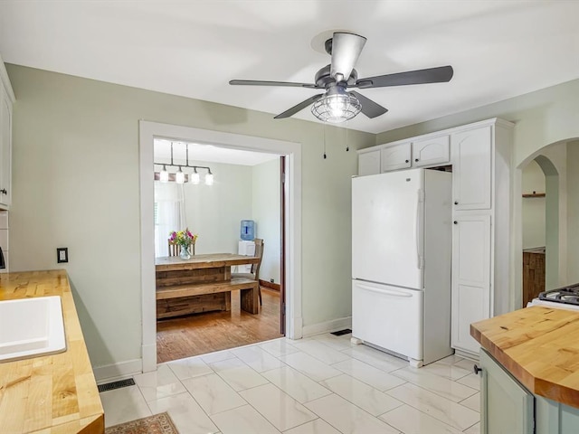 kitchen with freestanding refrigerator, wood counters, ceiling fan, arched walkways, and white cabinets