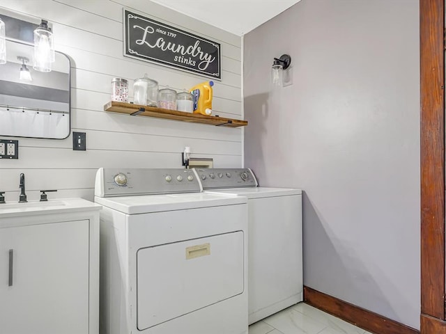 clothes washing area featuring washing machine and clothes dryer, light marble finish floors, and wood walls