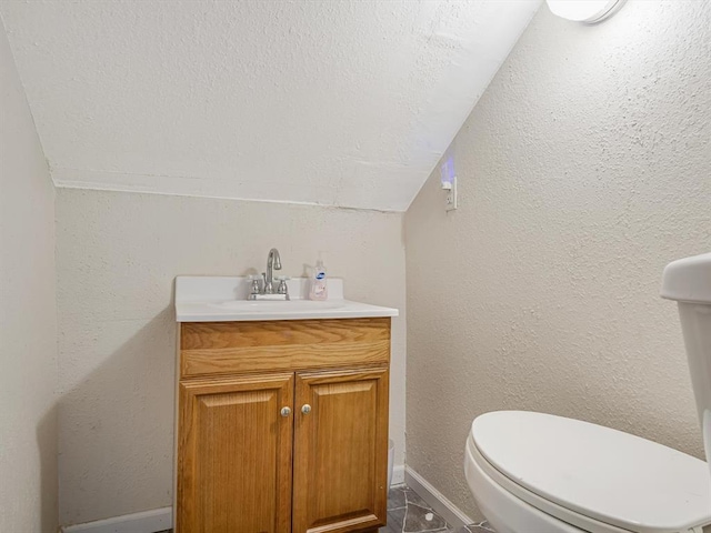bathroom with vanity, vaulted ceiling, toilet, and baseboards